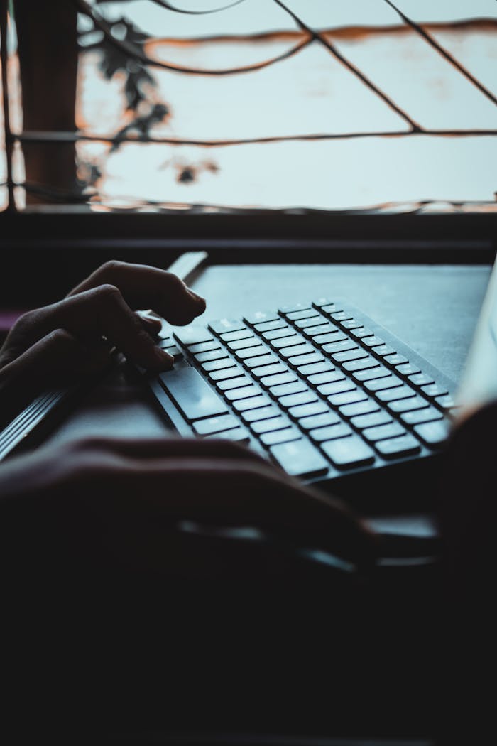 Close-up of hands typing on a laptop by a window with a nature view